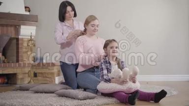 母亲一边给大女儿编辫子，一边给小女孩编辫子。 快乐的白种人家庭在一起休息